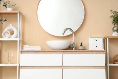 Banyodaki bej duvarın yanındaki çekmecelerde lavabo kasesi ve raf üniteleri.