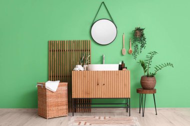 Lavabosu, çekmecesi ve yeşil duvarın yanında katlanır ekranı olan şık bir banyo.