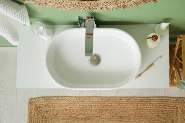 Modern lavabo, bir şişe sıvı sabun ve diş fırçası banyoda yeşil duvarın yanındaki çekmecelerde.