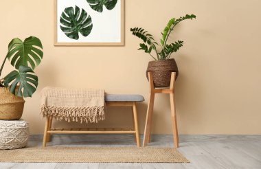 Bankta, odada bej duvarın yanında Monstera yaprakları ve bitkileri olan bir çerçeve.