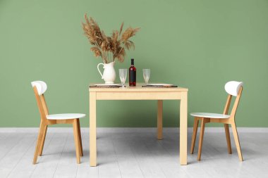 Yemek masası, vazo dolusu otlar ve şarap şişesi odada.