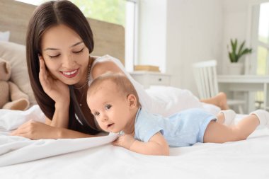 Güzel, genç, mutlu bir Asyalı anne ve tatlı bebeği evde yatakta yatıyor.