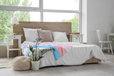 Geniş yataklı, transseksüel bayraklı ve pencere kenarındaki komodinli modern yatak odası.