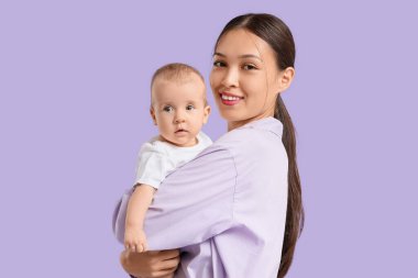 Güzel, genç, mutlu, Asyalı bir anne. Mor arka planda küçük bebeği var.