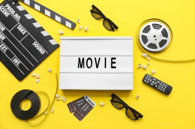 Sinema biletleri, film makaraları ve sarı arka planda uzaktan kumandalı film alkışları.