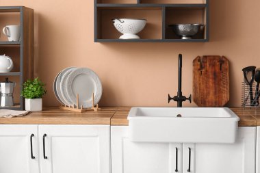 Seramik lavabo, güzel mutfaktaki bej duvarın yanındaki ahşap tezgahta.