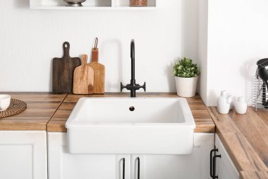 Mutfaktaki beyaz duvarın yanındaki ahşap tezgahta lavabo.