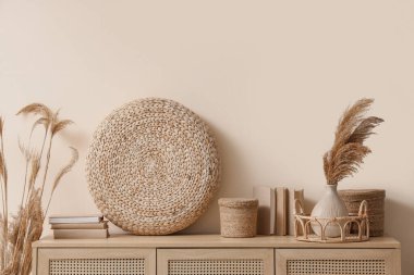 Bej duvarın yanındaki klozette farklı ev dekoru ve kuru kamış vazosu var.