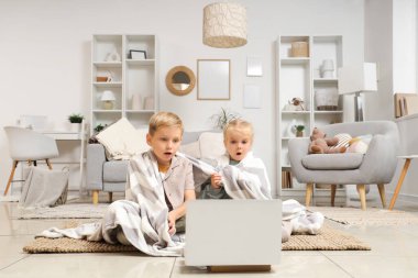 Evde dizüstü bilgisayar kullanan ekose elbiseli küçük bir kız ve oğlan.