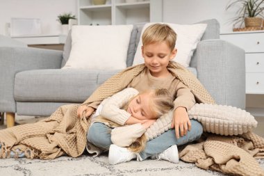 Küçük bir çocuk ve kız kardeşi evde ekoseyle uyuyorlar.