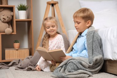 Ekoseli kumaş altında küçük bir çocuk ve kız evde yerde kitap okuyorlar.