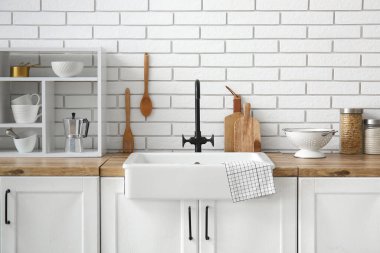 Beyaz seramik lavabo ve raf ünitesi mutfaktaki beyaz tuğla duvarın yanındaki ahşap tezgahta.