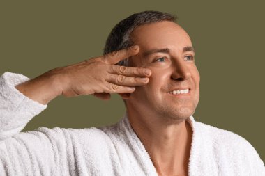 Bornozlu mutlu adam yeşil arka planda yüz geliştirme egzersizi yapıyor.