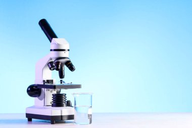 Modern mikroskop ve beyaz masada sıvı bulunan laboratuvar şişesi.