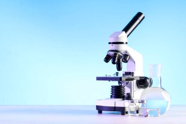 Modern mikroskop, ampuller ve beyaz masa üzerinde sıvı bulunan laboratuvar şişesi.