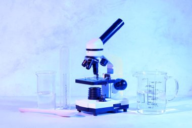 Modern mikroskop, kaşık ve mavi zemin üzerinde sıvı bulunan laboratuvar bardakları.