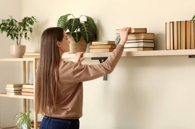 Oturma odasındaki raftan kitap alan genç bir kadın.