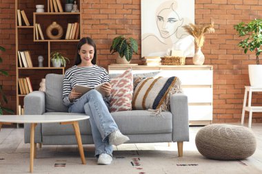 Genç bir kadın kanepede oturuyor ve oturma odasında kitap okuyor.