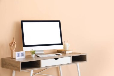 Ofisteki bej duvarın yanında modern bilgisayar, saat ve kırtasiye ile şık bir iş yeri