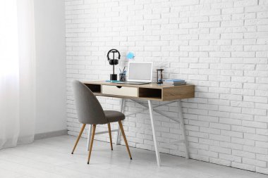 Modern dizüstü bilgisayarı, kulaklığı ve beyaz tuğla duvarın yanındaki koltuğu olan şık bir iş yeri.