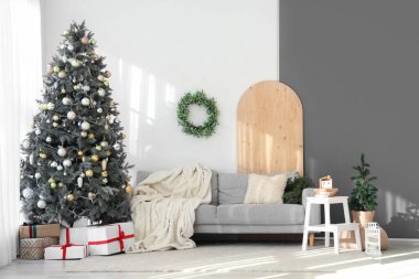Şık oturma odasının içinde kanepe, süslü Noel ağacı ve beyaz duvarda ökseotu çelengi var.