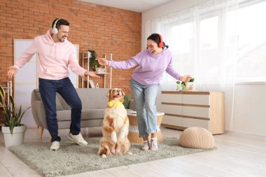 Evde kulaklıklı genç bir çift ve Avustralya çoban köpeği dans ediyorlar.