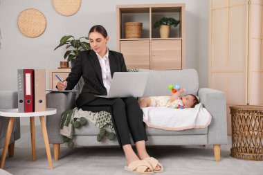 Genç mutlu iş annesi evde dizüstü bilgisayar ve küçük bebekle çalışıyor.