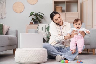 Bilgisayarlı genç mutlu anne cep telefonuyla konuşuyor ve evde küçük bebek var.