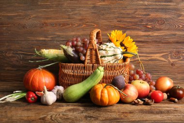 Tahta arka planda farklı taze sebzeler, meyveler ve ayçiçekli bir sepet. Hasat festivali