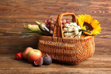 Tahta arka planda farklı taze sebzeler, meyveler ve ayçiçekli bir sepet. Hasat festivali