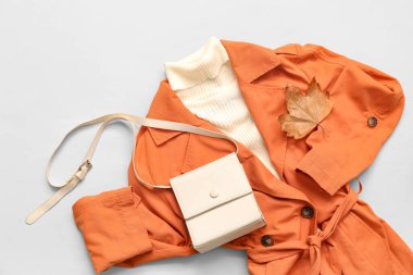 Beyaz arka planda ceket, süveter ve sonbahar yapraklı şık bir kadın çantası.