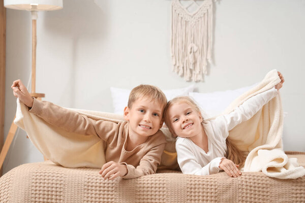 Little brother and sister lying on bed under plaids at home