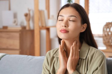 Genç Asyalı kadın tiroid bezini evde muayene ediyor, yakın plan.