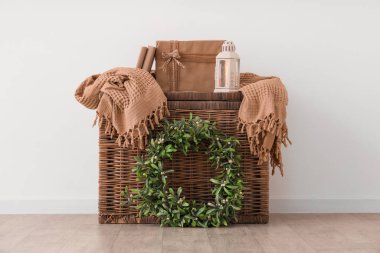 Beyaz duvarın yanında dekor ve ökseotu çelengi olan sepet.