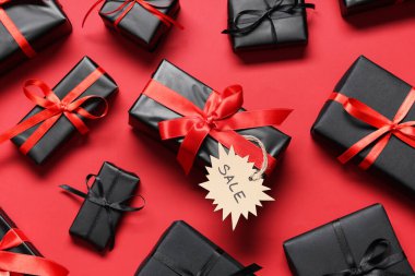 Kırmızı arka planda etiketli alışveriş çantası ve hediye kutuları. Kara Cuma indirimi. Üst görünüm