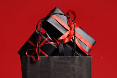 Kırmızı arka planda hediye kutuları olan bir alışveriş çantası. Kara Cuma indirimi. Yakın çekim.