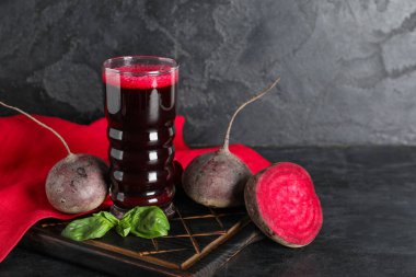 Siyah arka planda fesleğenli ve sebzeli bir bardak taze pancar suyu.