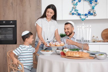 Mutlu aile, neşeli mutfakta lezzetli çöreklerle yemek yiyor. Hanuka kutlaması