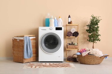 Modern çamaşır makinesi, çamaşır sepeti, raf ünitesi ve dekoratif ağaç.