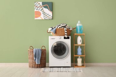 Modern çamaşır makinesi, çamaşır deterjanı ve sepeti olan raf ünitesi.