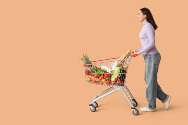 Güzel, genç, mutlu, bej arka planda alışveriş arabası olan bir kadın.