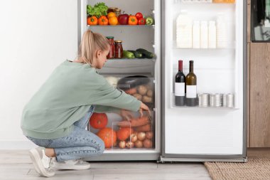 Genç bir kadın evdeki modern buzdolabından yemek seçiyor.
