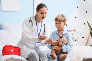 Suçiçeği hastası küçük bir çocuk ve yatak odasında termometreye bakan bir doktor.