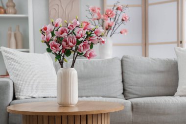 Sıcak kanepe ve vazodaki manolya çiçekleri odadaki sehpanın üzerinde.