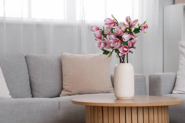 Sıcak kanepeler ve vazodaki manolya çiçekleri odadaki sehpanın üzerinde.