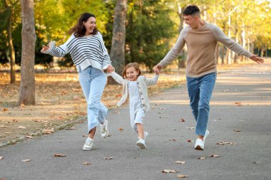 Mutlu bir aile güzel bir sonbahar parkında birlikte koşuyor.