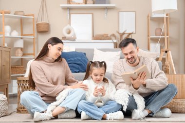 Mutlu aile ve kızları süveter giyip evde yerde bir fincan süt kitabı okuyorlar.
