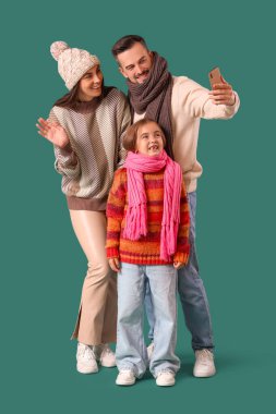 Mutlu bir aile ve yeşil arka planda süveter giyen kızları selfie çekiyorlar.