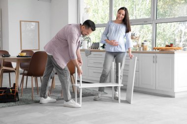 Mutlu hamile çift mutfaktaki raf ünitesini kuruyor.