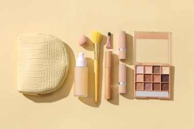 Sarı arka planda farklı makyaj ürünleri olan kozmetik çanta.